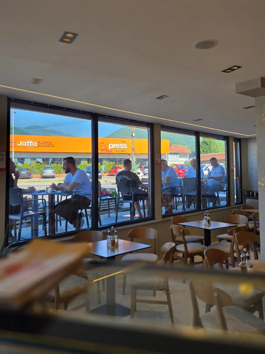 Ambienti i brendshëm i restorantit me tavolina dhe dritare drejt rrugës