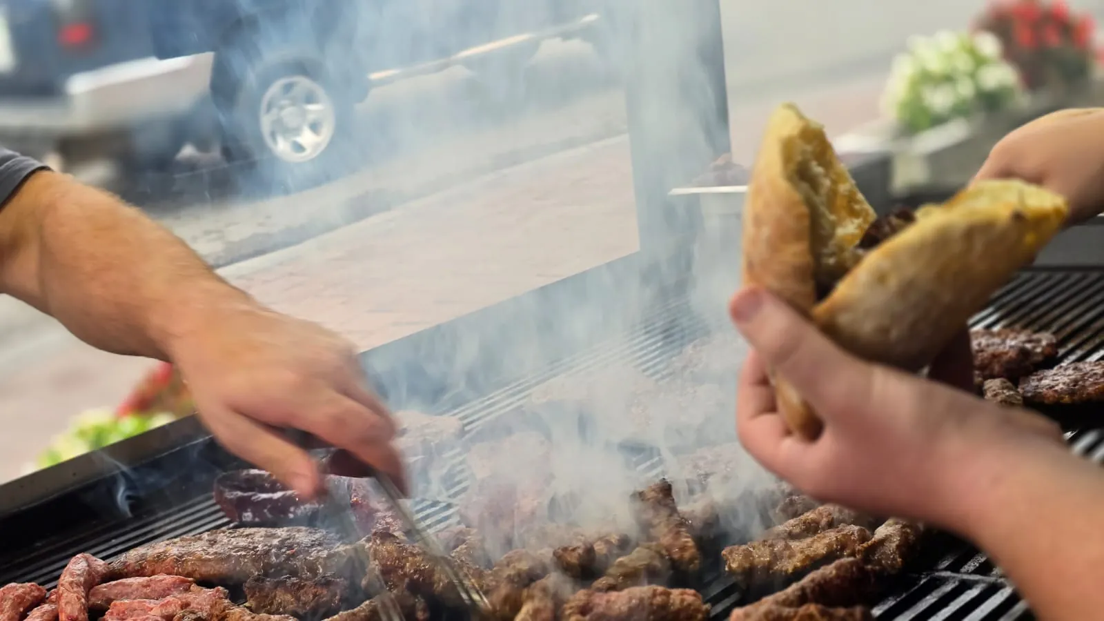 Qebapa duke u pjekur mbi prush druri dhe një dorë që mban bukë të ngrohtë te Jeta 2000 Grill House